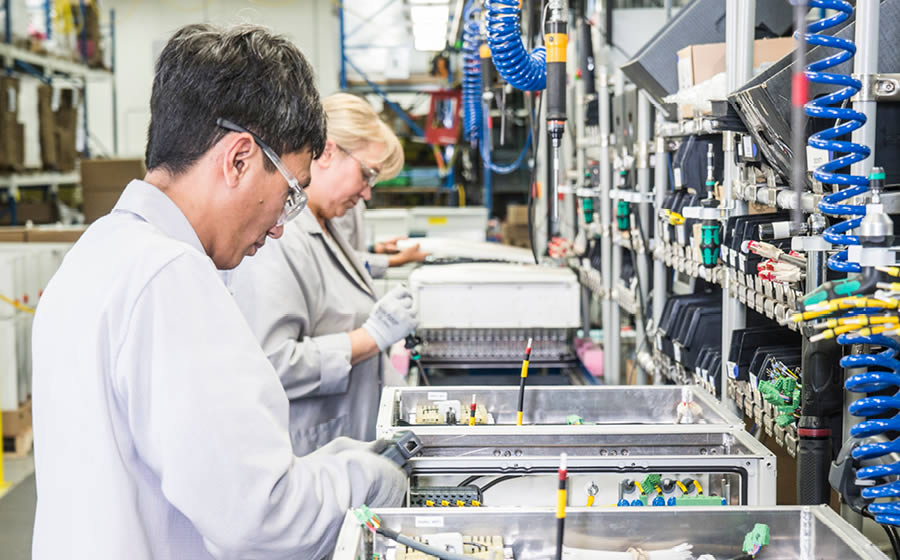 Melitron employees with safety glasses working on the electro-mechanical assembly line.