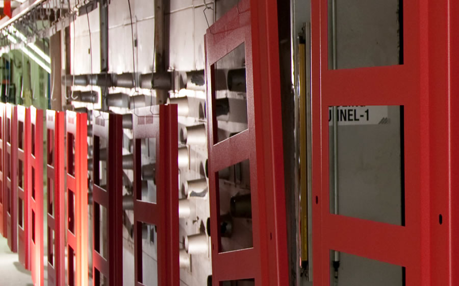 A line of metal enclosure panels on hooks hang to dry after treatment with a red powder-coated finish.